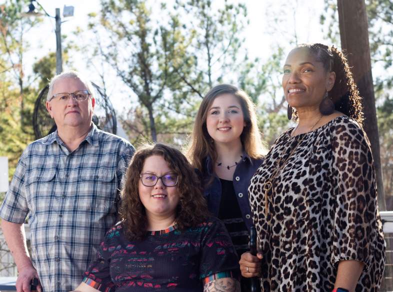 Pictured left to right, Doug, Kayla, Ireland and Kim, who live with NMOSD are grouped together looking happy and smiling towards the distance.